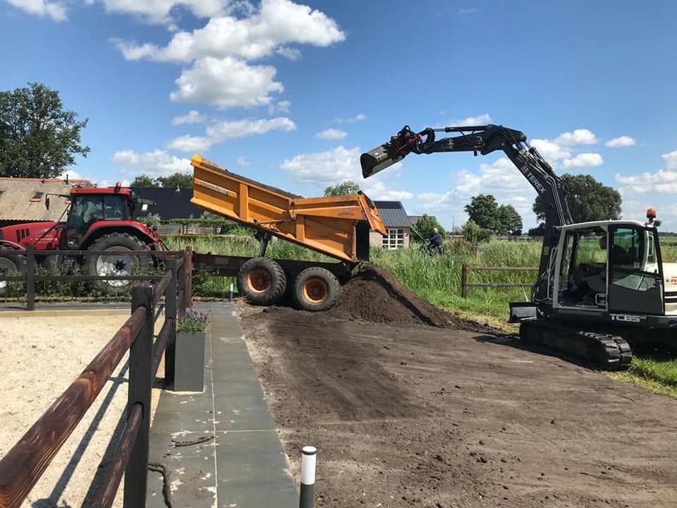Graafmachine laadt grond in een kiepwagen tijdens de aanleg van een tuin