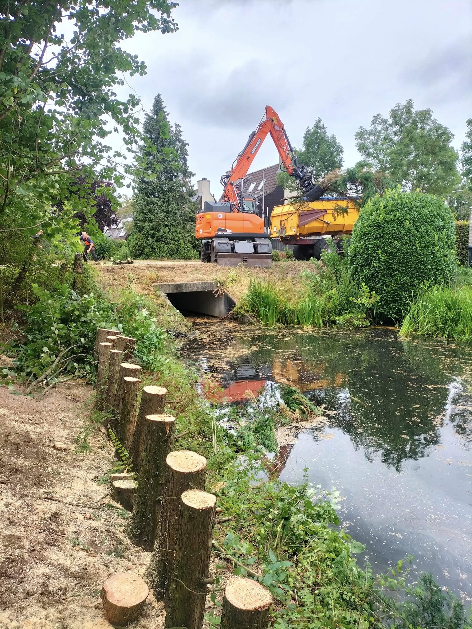 Graafmachine aan het werk bij een vijver in een groene tuin