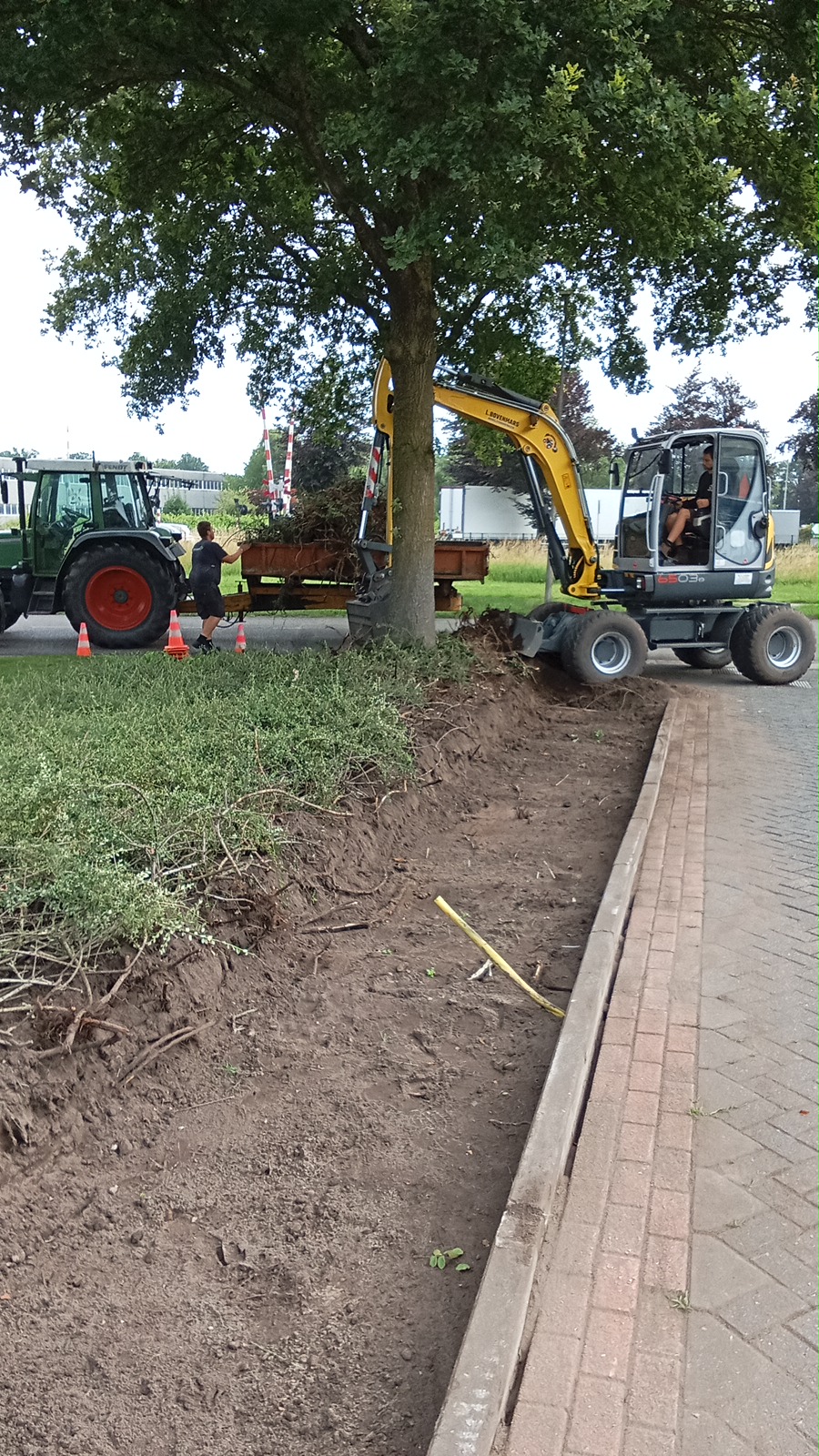 Graafmachine en tractor met aanhanger bij grondwerk langs een oprit